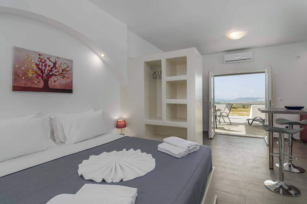 A hotel room with a bed, a painting, a desk, and a view of the outdoors.