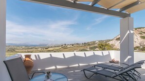A covered outdoor seating area with a table, chairs, and a vase. - Sunset Village (Milos)