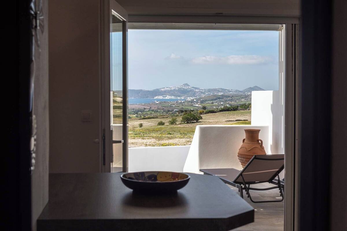 A balcony with a view of a mountainous landscape, a table with a bowl, and a chair.