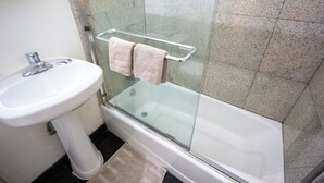 Ein Badezimmer mit weißem Waschbecken, einer Glaskabine zur Badewanne und einer Duschkabine.