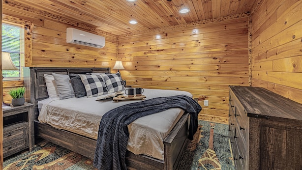 A wooden cabin-style bedroom with a bed, bedside table, lamp, and dresser.