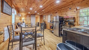A wooden cabin interior with a dining area, kitchen, and a refrigerator.