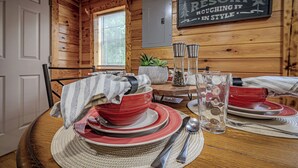 A wooden interior with a dining table set for four, featuring red and white plates, silverware, and a clear glass. A sign on the wall reads "WILDERNESS RESORT."