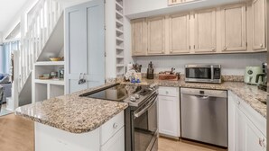 A modern kitchen with granite countertops, stainless steel appliances, and light wooden cabinets. - The Village 15D (Gulf Shores)