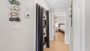 A laundry room with a washing machine and dryer, a power outlet, and a thermostat on the wall. - The Village 15D (Gulf Shores)