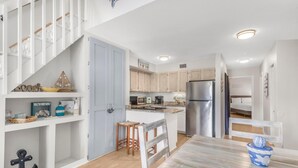 A modern kitchen with white cabinetry, a stainless steel refrigerator, and a wooden island with stools. - The Village 15D (Gulf Shores)