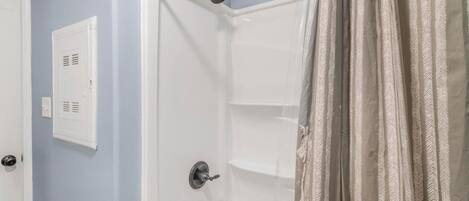 Una ducha con cabezal de ducha de mano, una puerta blanca con rejilla de ventilación y una cortina estampada.
