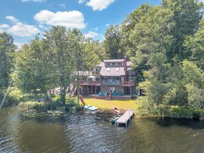 A lakeside property with a dock, boats, and a building with a deck and outdoor seating.