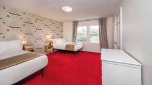 Ein Hotelzimmer mit rotem Teppich, zwei Betten, einem Nachttisch mit Lampe, einem Schminktisch und einem Fenster mit Vorhängen.