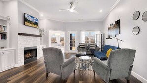 A modern living room with a fireplace, two grey armchairs, a coffee table, and a sofa.