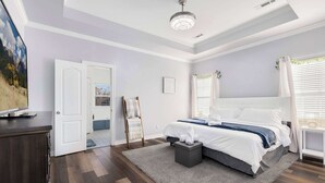 A bedroom with a large bed, a wooden dresser, a painting, and a ceiling fan.