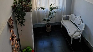 Un piccolo balcone chiuso con una sedia bianca, una pianta in vaso e un lampadario decorativo.