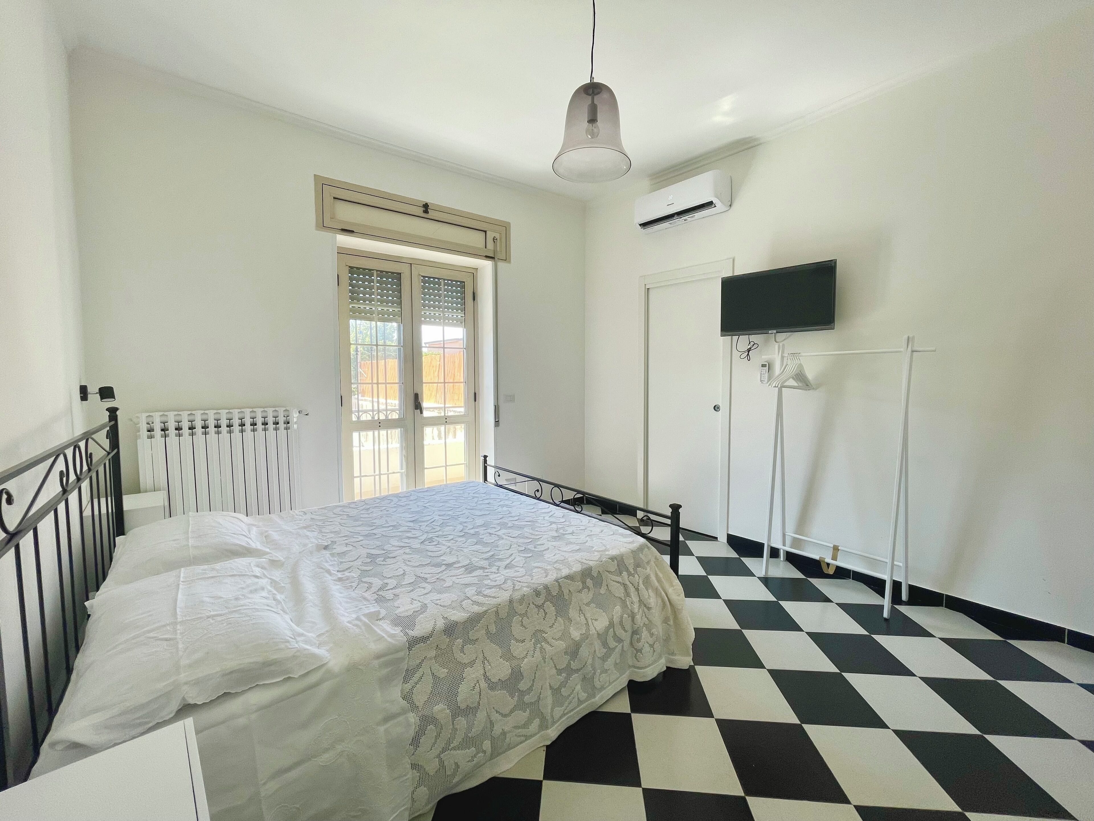 Une chambre à coucher avec un lit, un radiateur, une fenêtre, une porte, un téléviseur et un sol à carreaux.