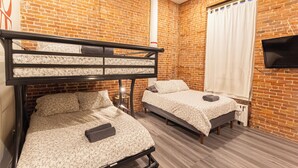 A room with two beds, a bunk bed, brick walls, a flat-screen TV, and a window with curtains. - Cozy STUDIO 1Full/2Twin beds near Empire State Building   (New York)