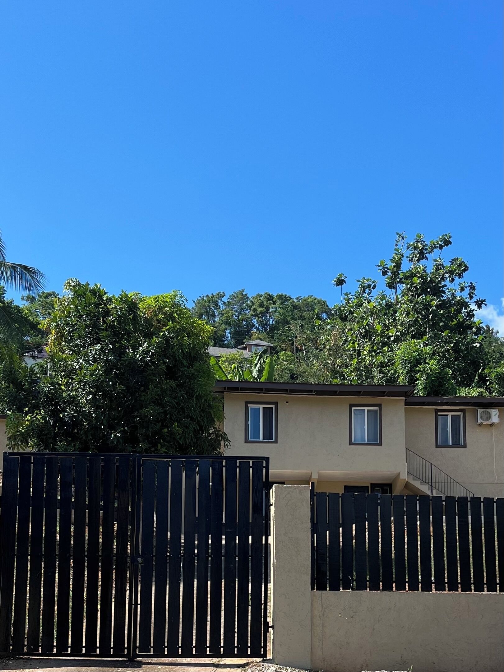 A residential building with a beige exterior, a black metal gate, and a clear blue sky.