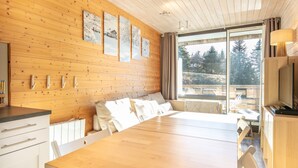 Un interior de madera con una mesa de comedor, sillas blancas, un sofá y un televisor.