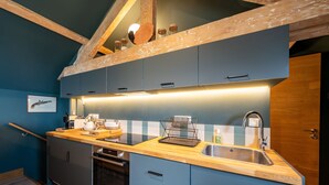 Una cocina compacta con armarios azules, una encimera de madera, un lavamanos de acero inoxidable y un horno empotrado.