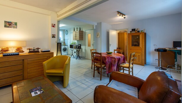 A living room with a dining area, wooden furniture, and a kitchen in the background.