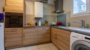 A modern kitchen with wooden cabinets, a built-in oven, a dishwasher, and a window with a view of a building.