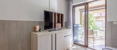 A modern room with a built-in TV, a small kitchenette, and a sliding glass door leading to an outdoor area.