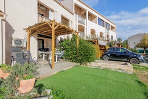 A multi-story building with a covered outdoor seating area, a car parked in front, and a well-maintained lawn. - Le Petit Paradis - Studio, plage à proximité (Aregno)