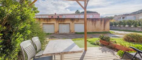 Eine Holzdielen-Terrasse mit Tisch und Stühlen, einer Pergola und Blick auf Gebäude im Hintergrund.