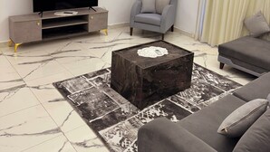 Een moderne woonkamer met een flatscreen televisie, een grijze bank en een salontafel met een kantje.