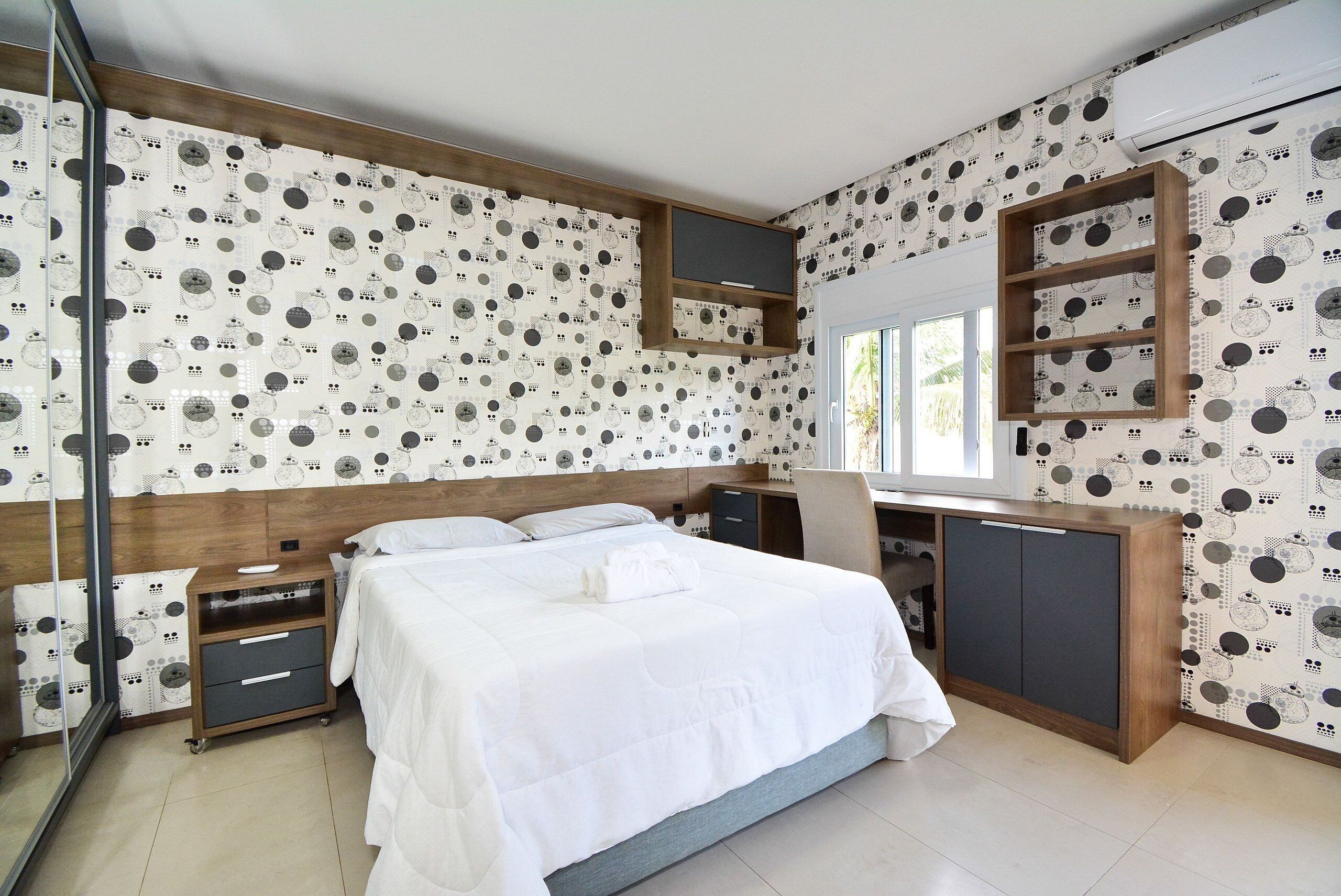 Un dormitorio con cama, escritorio, armario y televisor montado en la pared.