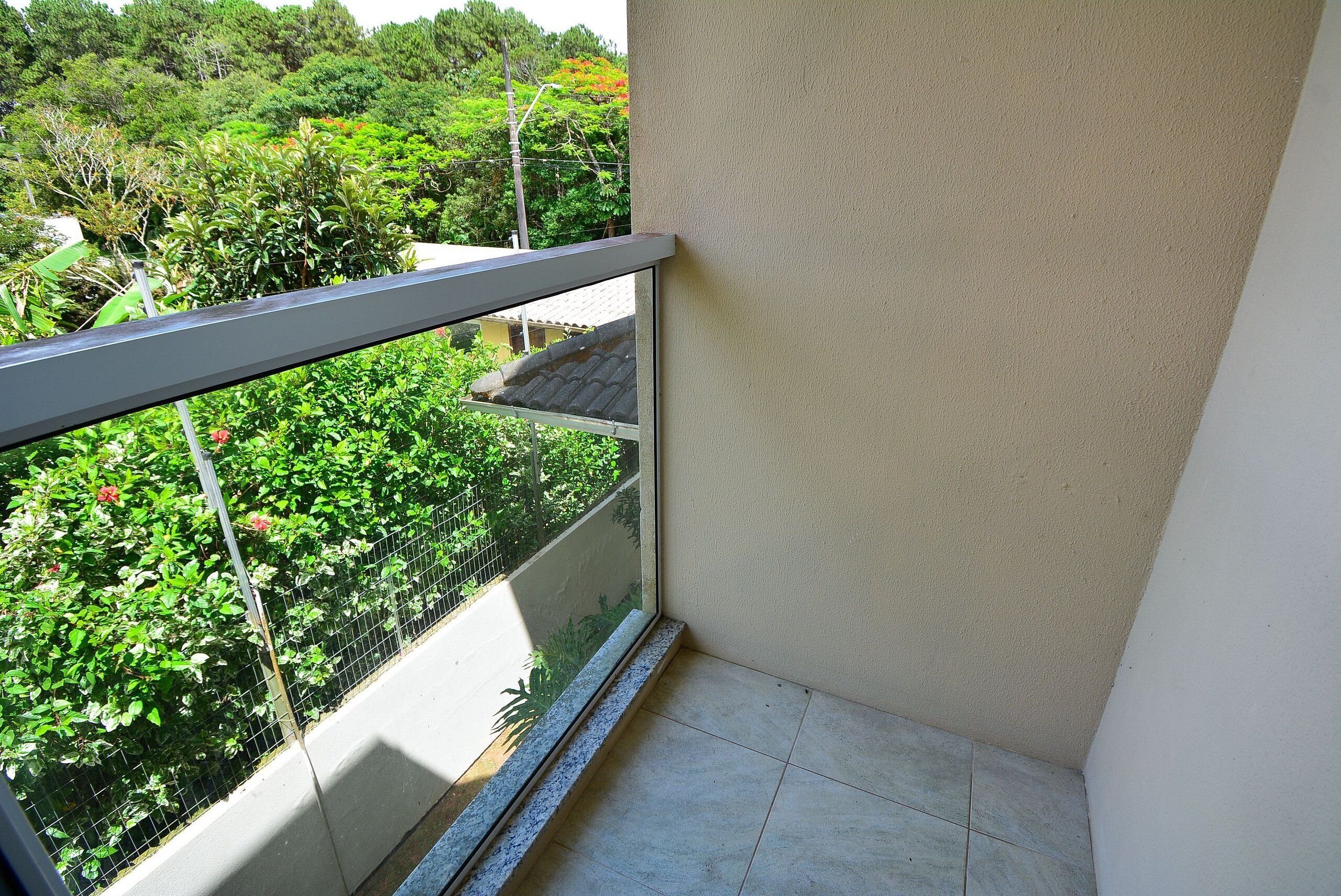 A corner of a room with a balcony overlooking a garden with various plants and a traditional building in the background.