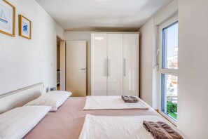 A hotel room with two beds, a wardrobe, and a window with a view.
