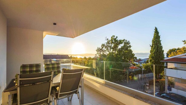 A balcony with a table and chairs, offering a view of the sea and surrounding buildings. - Holiday apartment with sea view (Njivice)