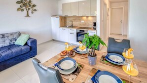 A modern living room with a sofa, dining table set with plates and glasses, and a kitchen in the background. - Holiday apartment with sea view (Njivice)