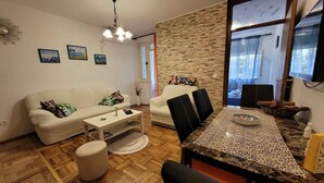 A living room with a sofa, coffee table, ottoman, and a dining table with chairs. There are wall-mounted pictures and a chandelier. - Holiday flat with balcony (Njivice)