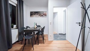 Un comedor moderno con una mesa y sillas de madera, un cuadro en la pared y vista a un pasillo que conduce a otra habitación.