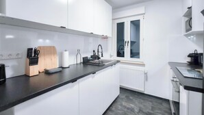 Una cocina moderna con armarios blancos, encimera negra y ventana con vidrio esmerilado.