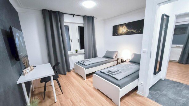 Una habitación moderna y luminosa con dos camas individuales, un escritorio y un televisor.