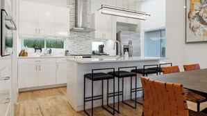 Una cocina moderna con armarios blancos, una isla central con taburetes y una mesa de comedor con sillas.