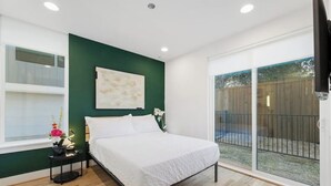 Un dormitorio con cama, mesita de noche, ventana y vista a un jardín trasero a través de una puerta corrediza de vidrio.