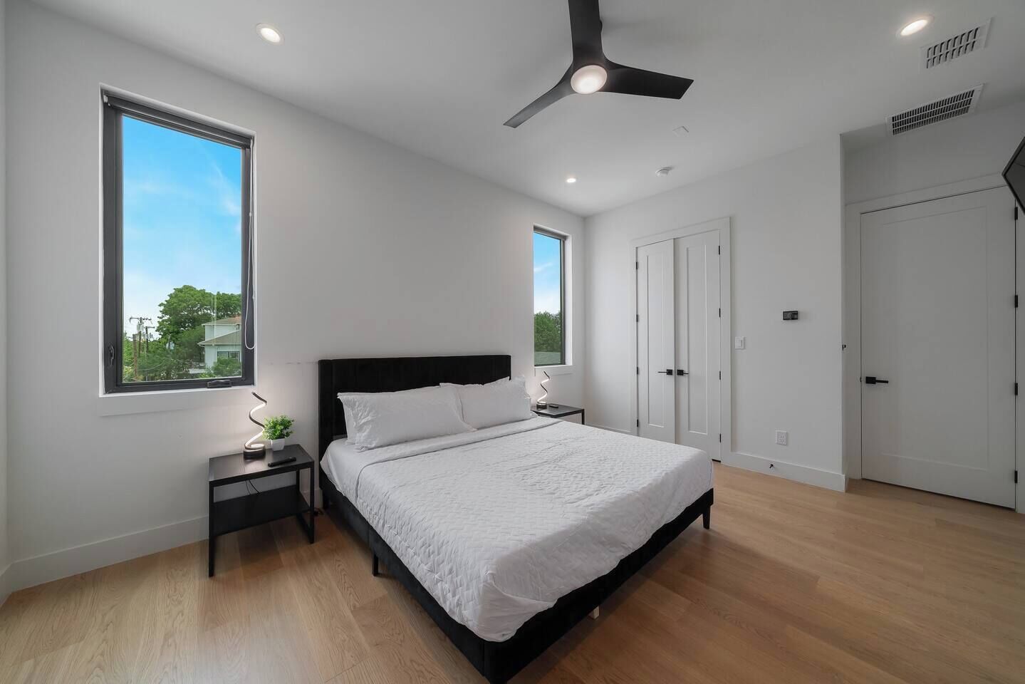 Quarto com cama, mesas de cabeceira, ventoinha no teto e janela.