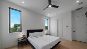 Une chambre à coucher avec un lit, des tables de chevet, un ventilateur de plafond et une fenêtre.