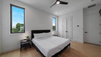 Quarto com cama, mesas de cabeceira, ventoinha no teto e janela.