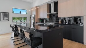 Une cuisine moderne dotée d’un îlot central, de plans de travail noirs, d’appareils électroménagers en acier inoxydable et d’armoires en bois clair.