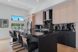 A modern kitchen with a central island, black countertops, stainless steel appliances, and light wood cabinets.