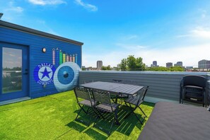 Una terraza en la azotea con un muro azul que presenta el logotipo de los Dallas Cowboys, una mesa con sillas y vistas del horizonte de la ciudad.