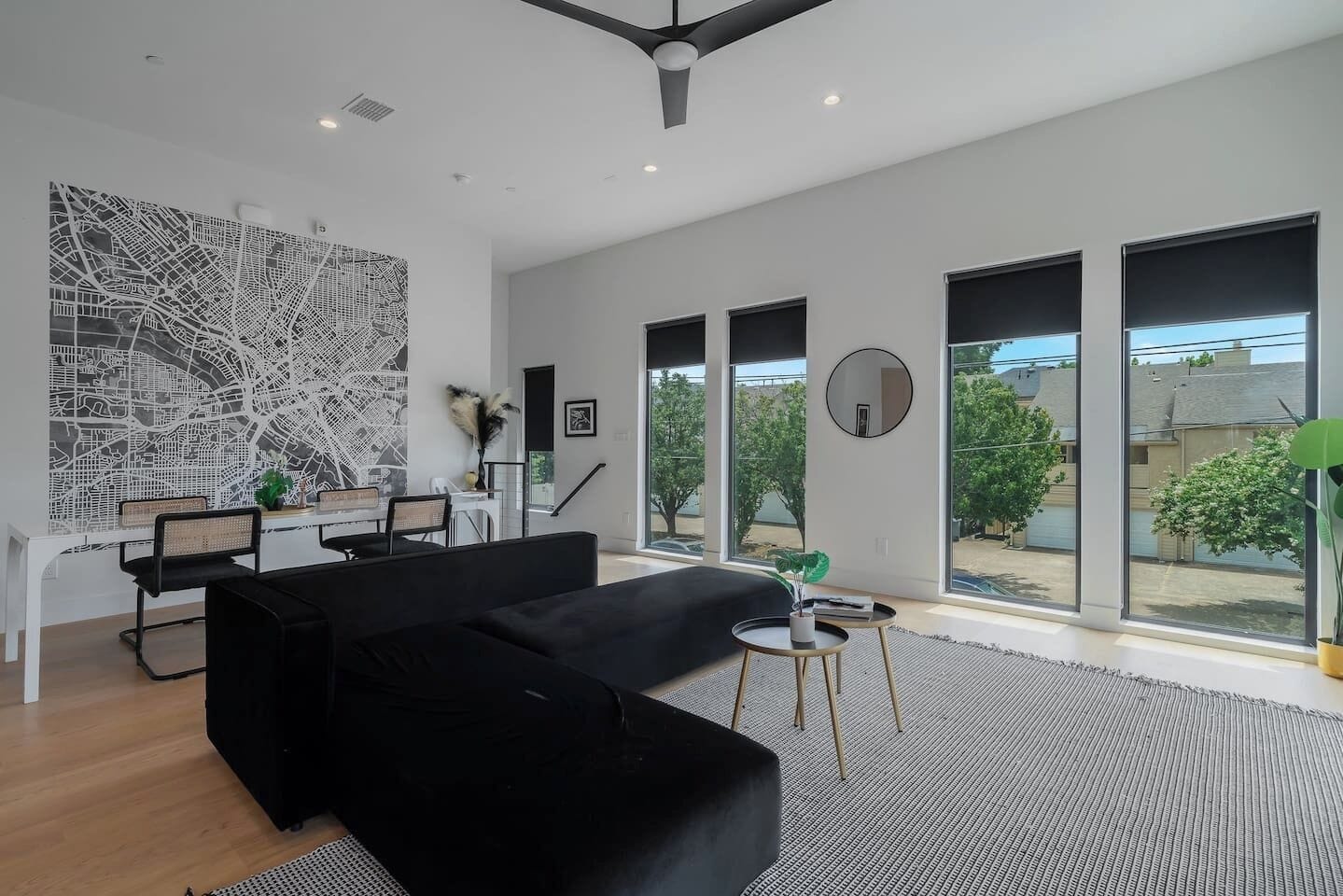 Uma sala de estar moderna com sofá preto, área de jantar e janelas amplas.