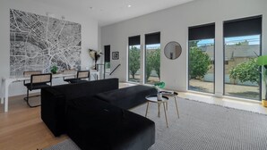 Un salon moderne avec un canapé noir, un coin repas et de grandes fenêtres.