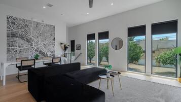 Uma sala de estar moderna com sofá preto, área de jantar e janelas amplas.