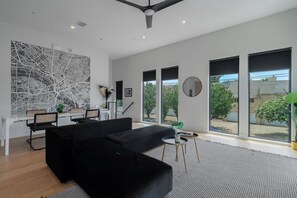 Una sala de estar moderna con un sofá negro, comedor y ventanas amplias.