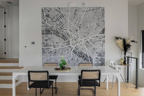 A modern dining area with a white table, black chairs, and a large abstract wall art piece.