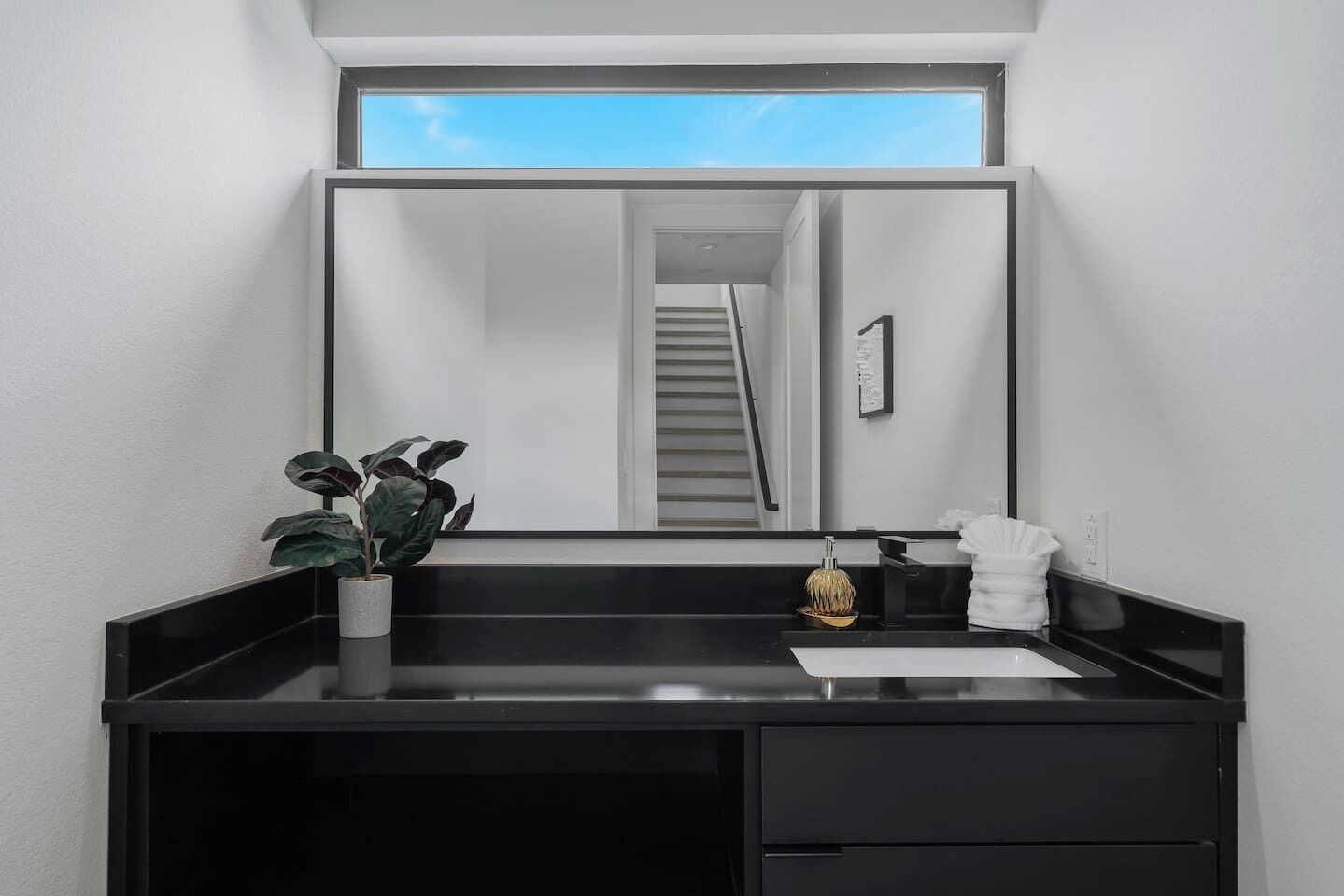 Um banheiro moderno com toucador preto, uma planta em vaso, um espelho e vista para uma escada.